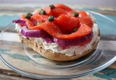 an open face sandwich with red onions and capers on a clear glass plate sitting on a wooden table