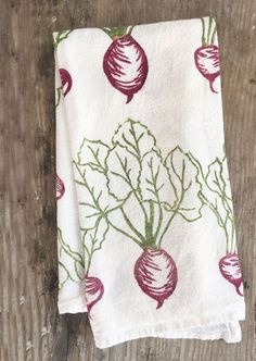 a kitchen towel with radishes on it sitting on a wooden table next to a knife