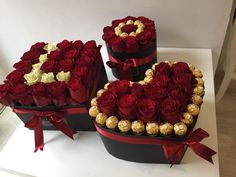 three heart shaped boxes filled with chocolates and roses on top of a white table