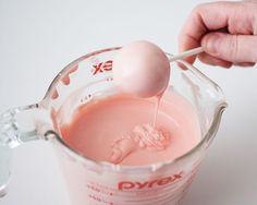 a person holding a spoon in a cup filled with pink liquid and an egg on top