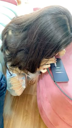 a woman with long hair sitting on top of a pink couch next to a phone