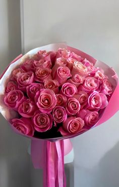 a bouquet of pink roses with a ribbon tied around the end, in front of a white wall