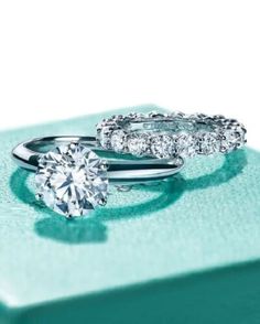 two engagement rings sitting on top of each other in front of a green box with diamonds