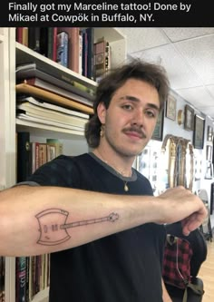 a man with a guitar tattoo on his arm in front of a bookshelf