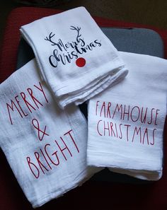 three white christmas towels with merry and bright words on them sitting on a red chair