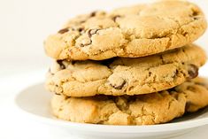 three chocolate chip cookies stacked on top of each other in a white plate against a white background