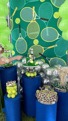 a tennis themed birthday party with blue cylinders and green balloons on the wall behind it