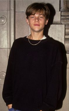 a young man standing in front of a building wearing a black sweater and white pants