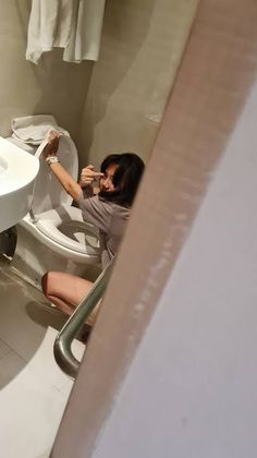 a woman sitting on a toilet in a bathroom next to a sink and towel rack