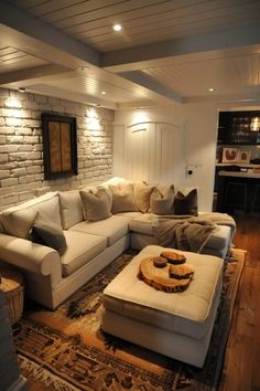 a living room with white couches and pillows on top of a rug in front of a brick wall