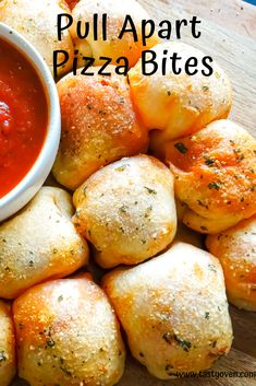 pizza bites are piled up on a cutting board with dipping sauce