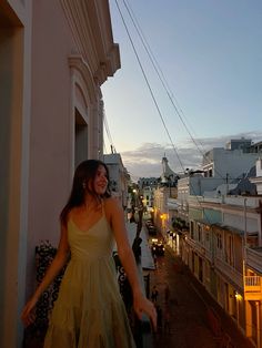 a woman in a yellow dress standing on a balcony at dusk with her arms outstretched