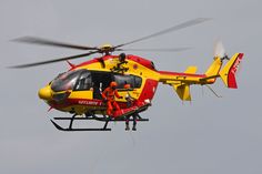 a red and yellow helicopter flying in the sky with two people on it's side