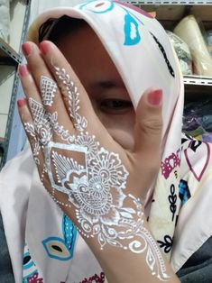 a woman is covered in white hendi on her hand and covering her face with both hands