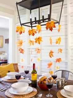 a dining room table with plates and wine glasses on it, next to fall leaves hanging from the ceiling