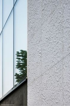 the side of a white building with trees reflected in it's glass window wall