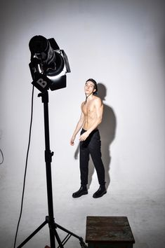 a shirtless man standing in front of a camera on a tripod with his hands behind him