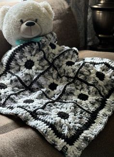 a white teddy bear sitting on top of a couch under a crocheted blanket