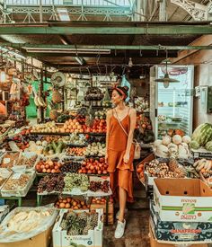 a woman standing in front of a market filled with fruits and vegetables