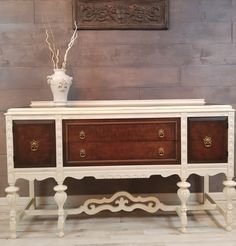 a white and brown dresser sitting on top of a wooden floor next to a vase