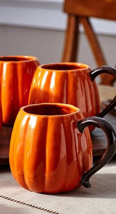 three orange coffee mugs sitting on top of a wooden tray next to each other