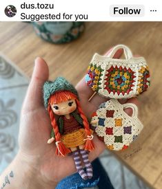 a hand holding three small crocheted items in it's palm, one with a doll and the other has a purse