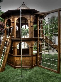 a wooden play set in the grass with a slide and climbing net attached to it