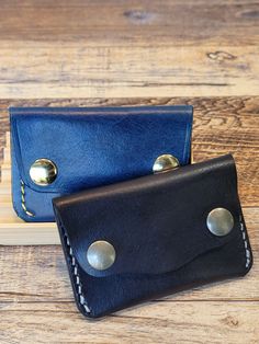 two black and blue leather wallets sitting on top of a wooden table next to each other