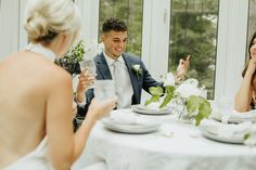 a man and woman sitting at a table with white flowers in front of them talking to each other