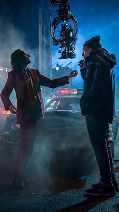 two men standing next to each other in front of a car on a city street