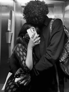 a man and woman hugging in an elevator while looking at their cell phones, black and white photograph