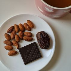 almonds, chocolate and nuts on a white plate next to a cup of tea