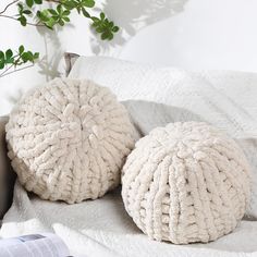 two white round poufces sitting on top of a bed next to a plant