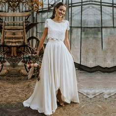 a woman standing in front of a greenhouse wearing a white wedding dress with short sleeves