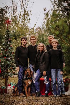 a group of people standing next to each other in front of a christmas tree with a dog