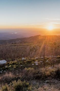 the sun is setting on top of a hill with cactus and rocks in the foreground