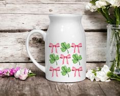 a white pitcher sitting on top of a wooden table next to some pink and green flowers