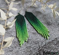 two pairs of green and black seed earrings on top of a gray rock next to leaves