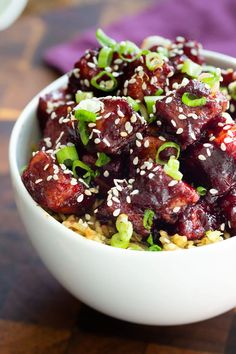 a white bowl filled with rice and meat covered in sesame seeds on top of a wooden table