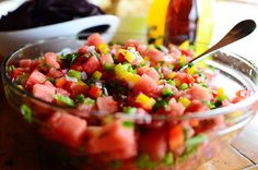 a glass bowl filled with watermelon and green onions next to a bottle of orange juice