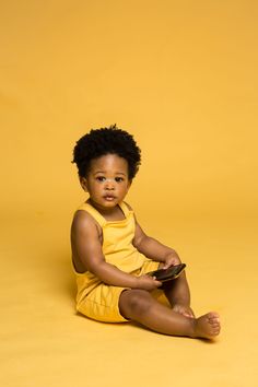 a small child sitting on the ground with a cell phone in his hand and wearing a yellow shirt