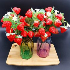 two vases filled with strawberries on top of a cutting board next to each other