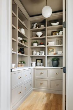 an open pantry with white cabinets and shelves filled with dishes, cups and vases