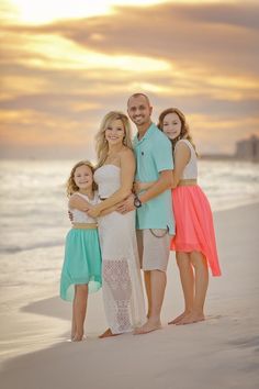 a family posing for a photo on the beach in front of the ocean at sunset