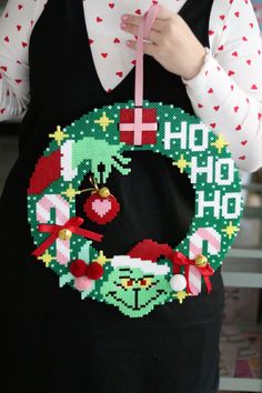 a woman is holding a cross stitch christmas wreath