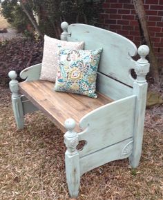 a wooden bench sitting in the grass next to a brick wall and tree with two pillows on it