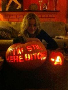 a woman sitting on a couch with two carved pumpkins