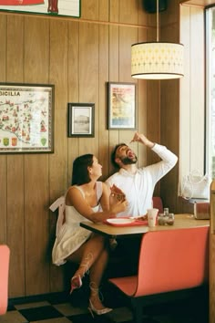 a man and woman sitting at a table in a restaurant, one pointing to the ceiling