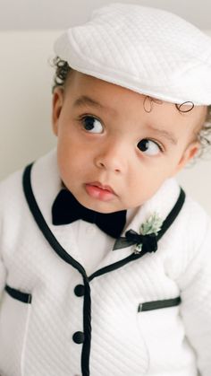 a baby wearing a white jacket and black bow tie with a hat on his head