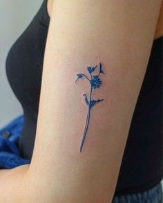 a small blue flower tattoo on the right side of the left arm and upper arm